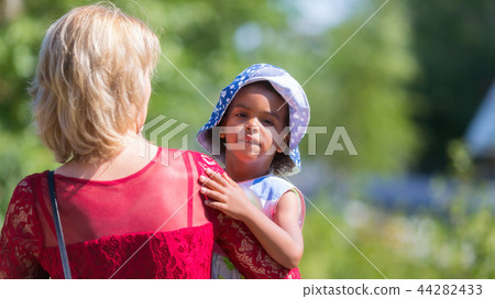 A white woman carries a black girl her shoulder. 44282433