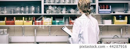 Serious female scientist writing on her clipboard Serious female scientist writing on her clipboard 44287916