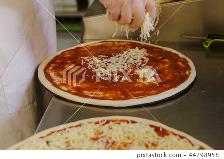Cheese being spread on tomato sauce on pizza base Cheese being spread on tomato sauce on pizza base 44298958