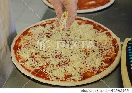 Cheese being spread on tomato sauce on pizza base Cheese being spread on tomato sauce on pizza base 44298959