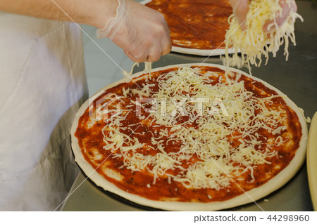 Cheese being spread on tomato sauce on pizza base Cheese being spread on tomato sauce on pizza base 44298960