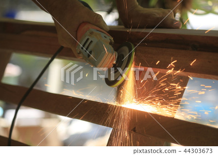 The carpenter works with the electric polisher. 44303673