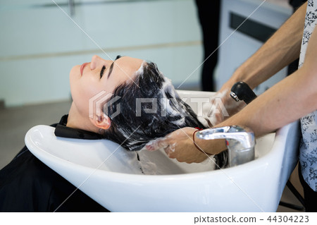beauty and people concept - happy young woman with hairdresser washing head at hair salon beauty and people concept - happy young woman with hairdresser washing head at hair salon 44304223