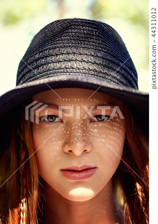 Portrait of a red-haired girl with long hair, in a black wide-brimmed hat.The sun makes freckles on 44311012