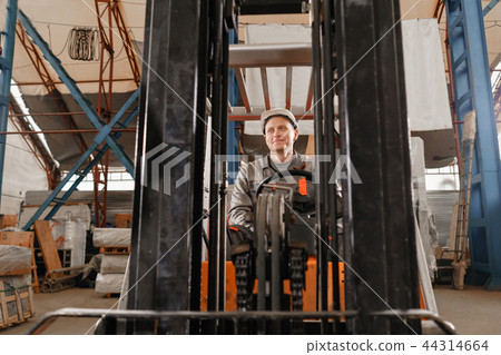 man driving a forklift through a warehouse in a factory. driver in uniform and protective helmet man driving a forklift through a warehouse in a factory. driver in uniform and protective helmet 44314664