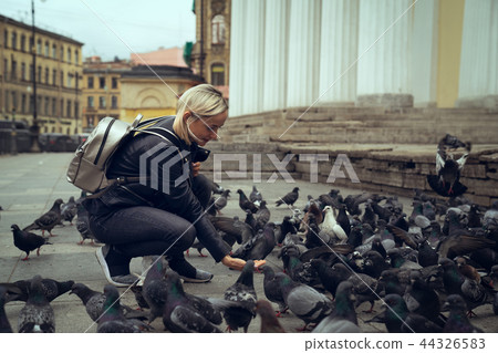 Young beautiful woman is feeding pigeons with bread crumbs in the town square on autumn day 44326583