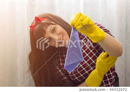 A brunette girl in yellow gloves holds a rag for cleaning 44332072