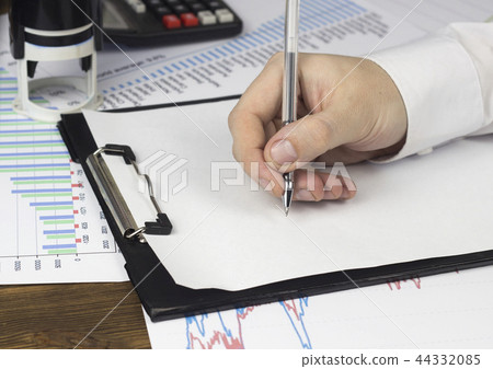 A man's hand holds a pen on a blank sheet, calculator, a seal A man's hand holds a pen on a blank sheet, calculator, a seal 44332085