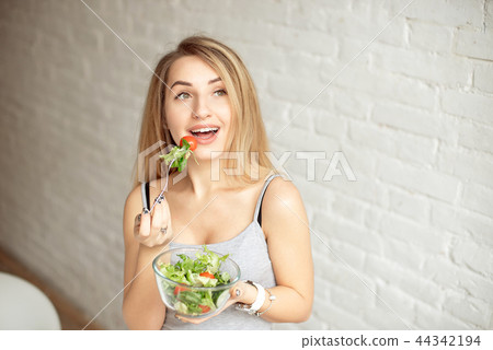 Attractive happy woman holding bowl of fresh vegetable salad in hands eating with the fork, enjoing Attractive happy woman holding bowl of fresh vegetable salad in hands eating with the fork, enjoing 44342194