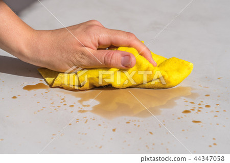 woman's hand cleaning spilled water on a cement floor with a yellow floor cloth dishcloth 44347058