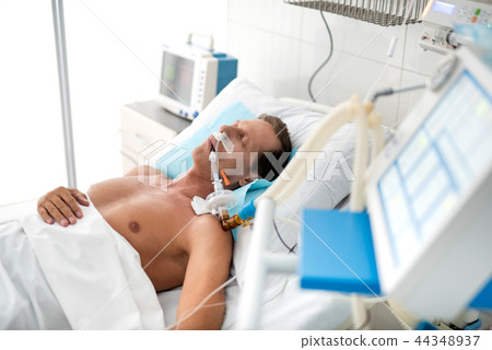Unconscious patient on mechanical ventilator lying in hospital bed 44348937