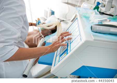 Doctor checking breathing machine while putting oxygen mask on patient 44350043
