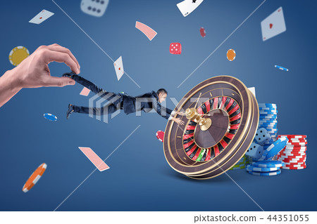 A huge hand tries to pull a small businessman away from a large casino roulette. A huge hand tries to pull a small businessman away from a large casino roulette. 44351055