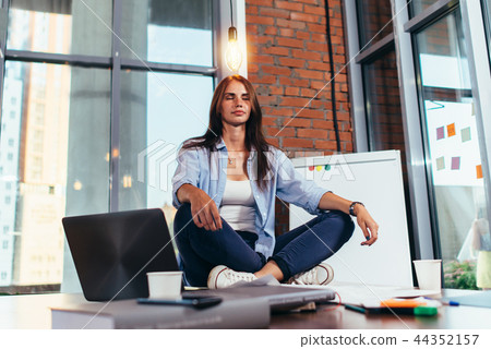 Female student sitting in lotus pose on table in her room meditating relaxing after studying and 44352157