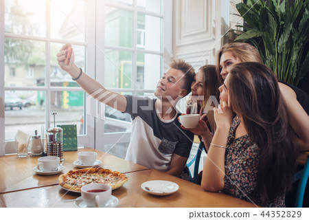 Group of cute teenagers taking selfie with cellphone while sitting in a restaurant with interior in Group of cute teenagers taking selfie with cellphone while sitting in a restaurant with interior in 44352829