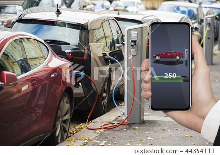 Hand with phone. Electric car charging point. Hand with phone. Electric car charging point. 44354111