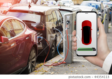 Hand with phone. Electric car charging point. Hand with phone. Electric car charging point. 44354113