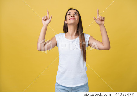 Happy young woman standing and pointing finger on copy space isolated over yellow gold wall 44355477