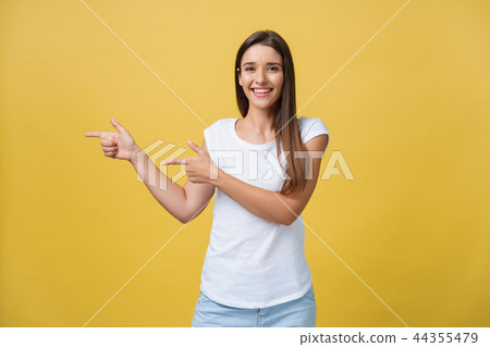 Happy young woman standing and pointing finger on copy space isolated over yellow gold wall 44355479