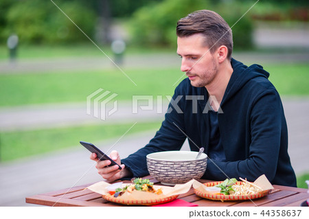 Young man eating take away noodles on the street Young man eating take away noodles on the street 44358637