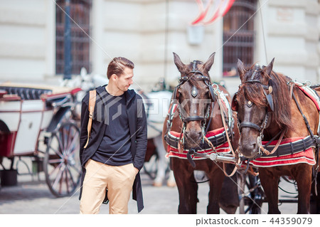 Tourist man enjoying a stroll through Vienna and looking at the two horses in the carriage 44359079