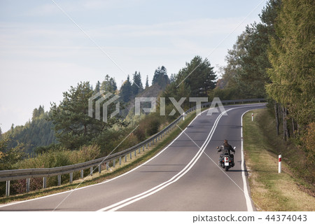 Biker in black leather outfit driving modern powerful motorcycle along sunny road on summer day. Biker in black leather outfit driving modern powerful motorcycle along sunny road on summer day. 44374043