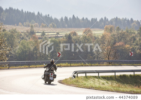 Biker in black leather outfit driving modern powerful motorcycle along sunny road on summer day. 44374089