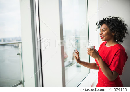 A woman standing by the window holding coffee cup, looking out. Copy space. 44374123