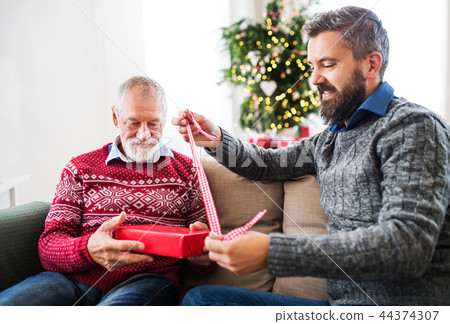 A senior father and adult son with a present sitting on a sofa at Christmas time. A senior father and adult son with a present sitting on a sofa at Christmas time. 44374307