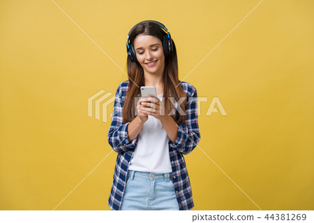 Beautiful young woman in headphones listening to music and dancing on yellow background. Beautiful young woman in headphones listening to music and dancing on yellow background. 44381269