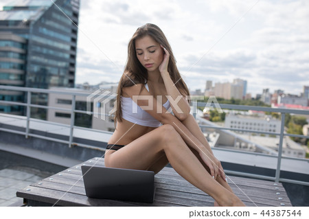 Young woman in a white top and panties sitting on the roof and using laptop. Young woman in a white top and panties sitting on the roof and using laptop. 44387544