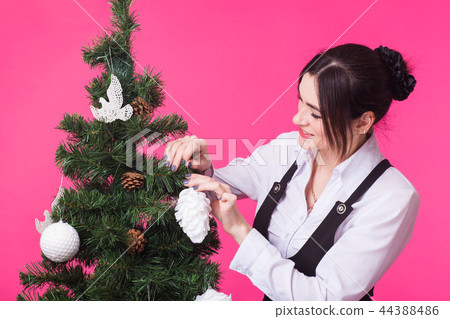 Christmas, holidays and people concept - young happy woman decorating christmas tree on pink 44388486