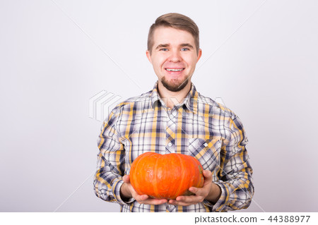 Holiday, autumn and people concept - Smiling man holding small orange pumpkin over white background Holiday, autumn and people concept - Smiling man holding small orange pumpkin over white background 44388977