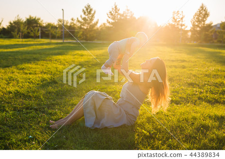 Young woman with boy on the meadow on a sunny day. Happy family on summer sunset. Mother with baby. 44389834
