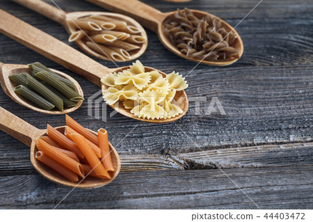 A set of raw pastas on spoons on a wooden table 44403472