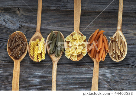 A set of raw pastas on spoons on a wooden table 44403588