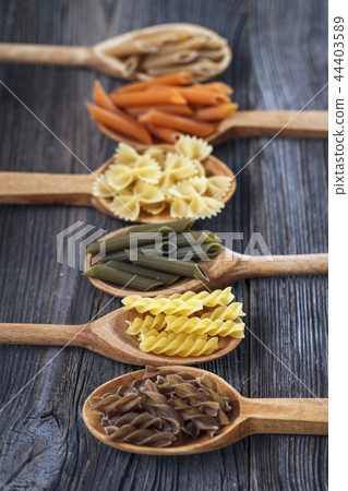 A set of raw pastas on spoons on a wooden table 44403589