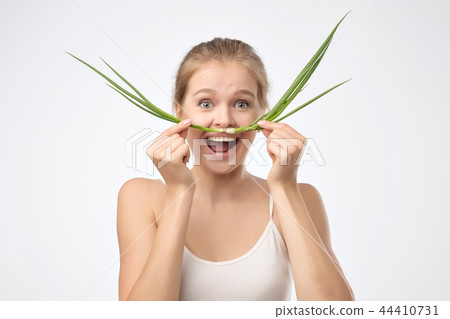 Portrait of beautiful blond woman in a white shirt holding a green onion like a mustache near mouth Portrait of beautiful blond woman in a white shirt holding a green onion like a mustache near mouth 44410731