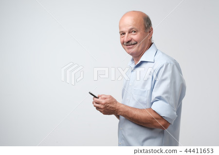 Mature businessman with mustache in blue shirt using phone to write sms. Mature businessman with mustache in blue shirt using phone to write sms. 44411653