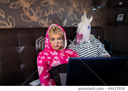 Serious girl is lying on bed with strange boyfriend in funny mask Serious girl is lying on bed with strange boyfriend in funny mask 44417036