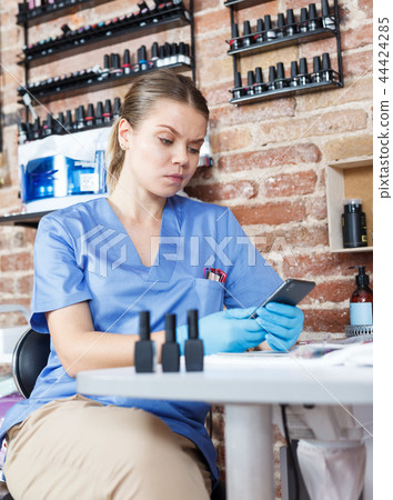 Professional nail master using phpone at working place in salon 44424285