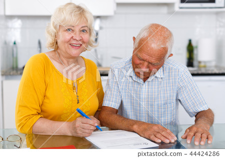 Smiling mature couple in home interior filling up documents 44424286