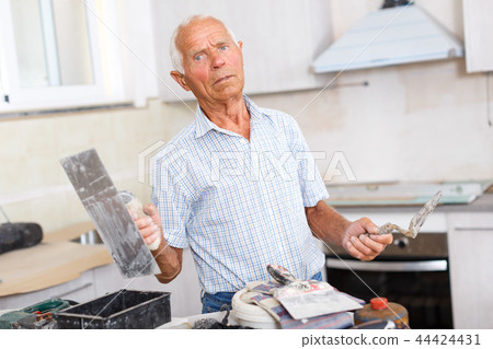 Senior man puttying walls Senior man puttying walls 44424431
