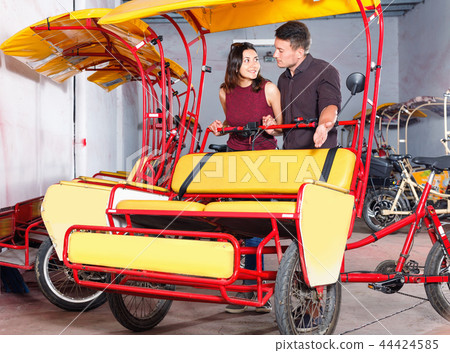 Cheerful girl with boyfriend wanting to hire touristic trishaw for urban trip Cheerful girl with boyfriend wanting to hire touristic trishaw for urban trip 44424585