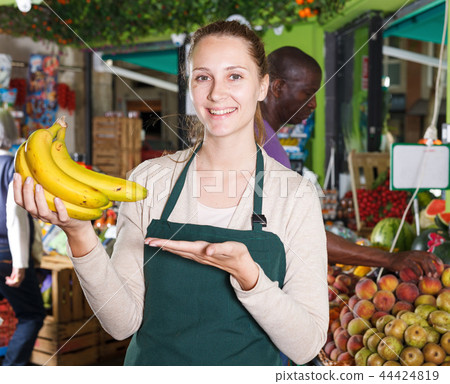 Portrait of seller female who is holding bananas on her workplace 44424819