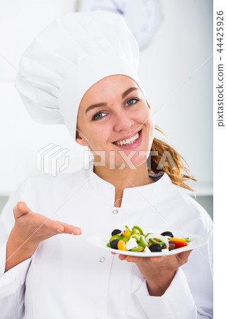portrait of young coosie woman showing salad at kitchen 44425926