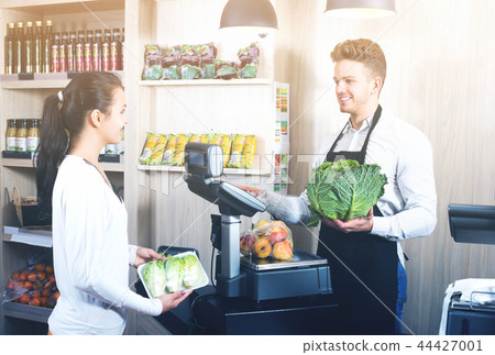 Seller assisting customer to weigh purchases Seller assisting customer to weigh purchases 44427001