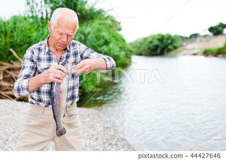 Adult fisherman removing catch from hook Adult fisherman removing catch from hook 44427646