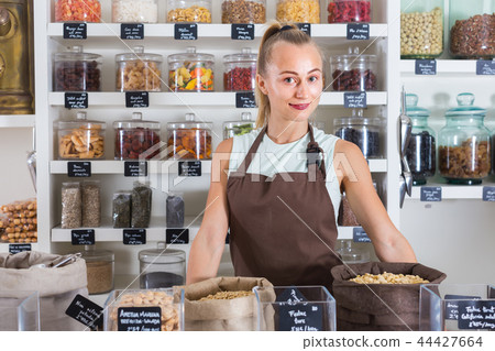 Female seller is working near showcase with dried fruits 44427664