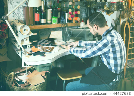 male worker sewing stitches on belt in leather workshop male worker sewing stitches on belt in leather workshop 44427688